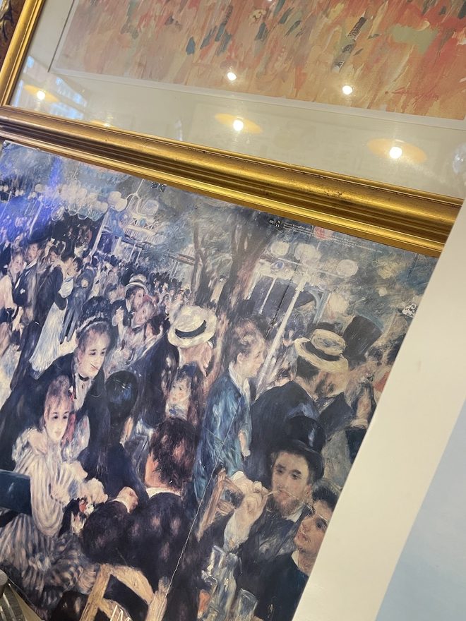 A large framed reproduction of a Renoir-style cafe painting on the wall