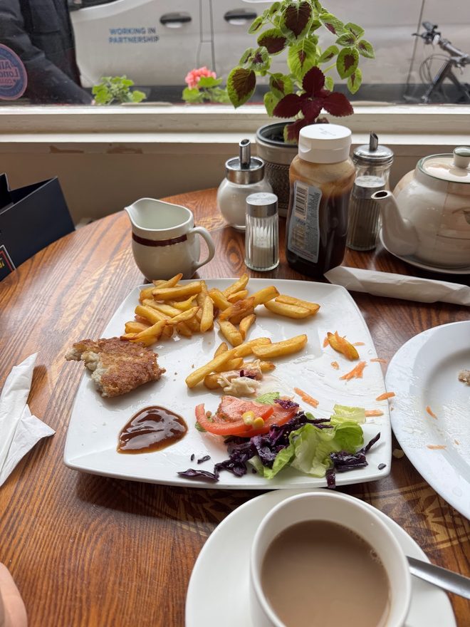 A plate of chips and salad with a cup of tea at a window table