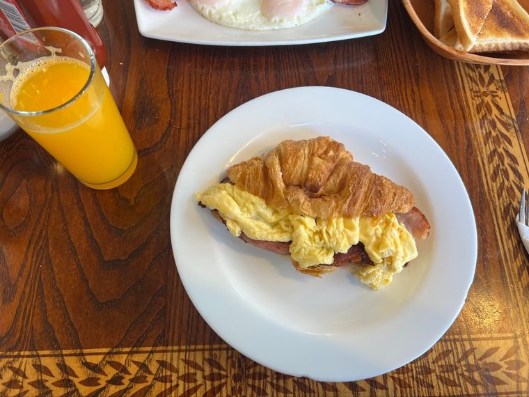 A croissant filled with scrambled egg beside orange juice